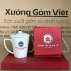 Cốc sứ in logo Trường Tiểu Học Hoa Lư dáng vát có nắp màu trắng họa tiết sen xanh XG-LS149