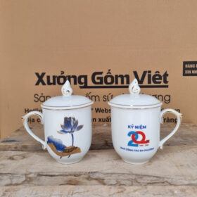 Cốc sứ in logo kỷ niệm 20 năm Ban công tác đa phương dáng ngọn lửa có nắp màu trắng họa tiết hoa sen xanh kẻ chì vàng XG-LS184