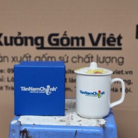 Cốc sứ Bát Tràng in logo Tân Nam Chinh - Vietnam Logistics dáng trụ cao có nắp họa tiết hoa hướng dương màu trắng XG-LS195